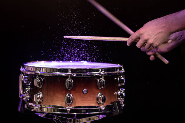 Drum sticks hitting snare drum with splashing water on black background under studio lighting close up.